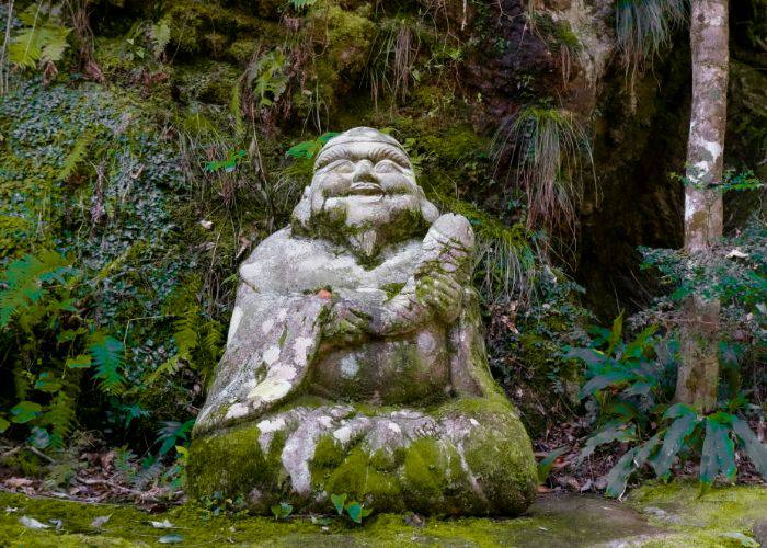 A stone statue of Ebisu holding a fish, covered in moss.